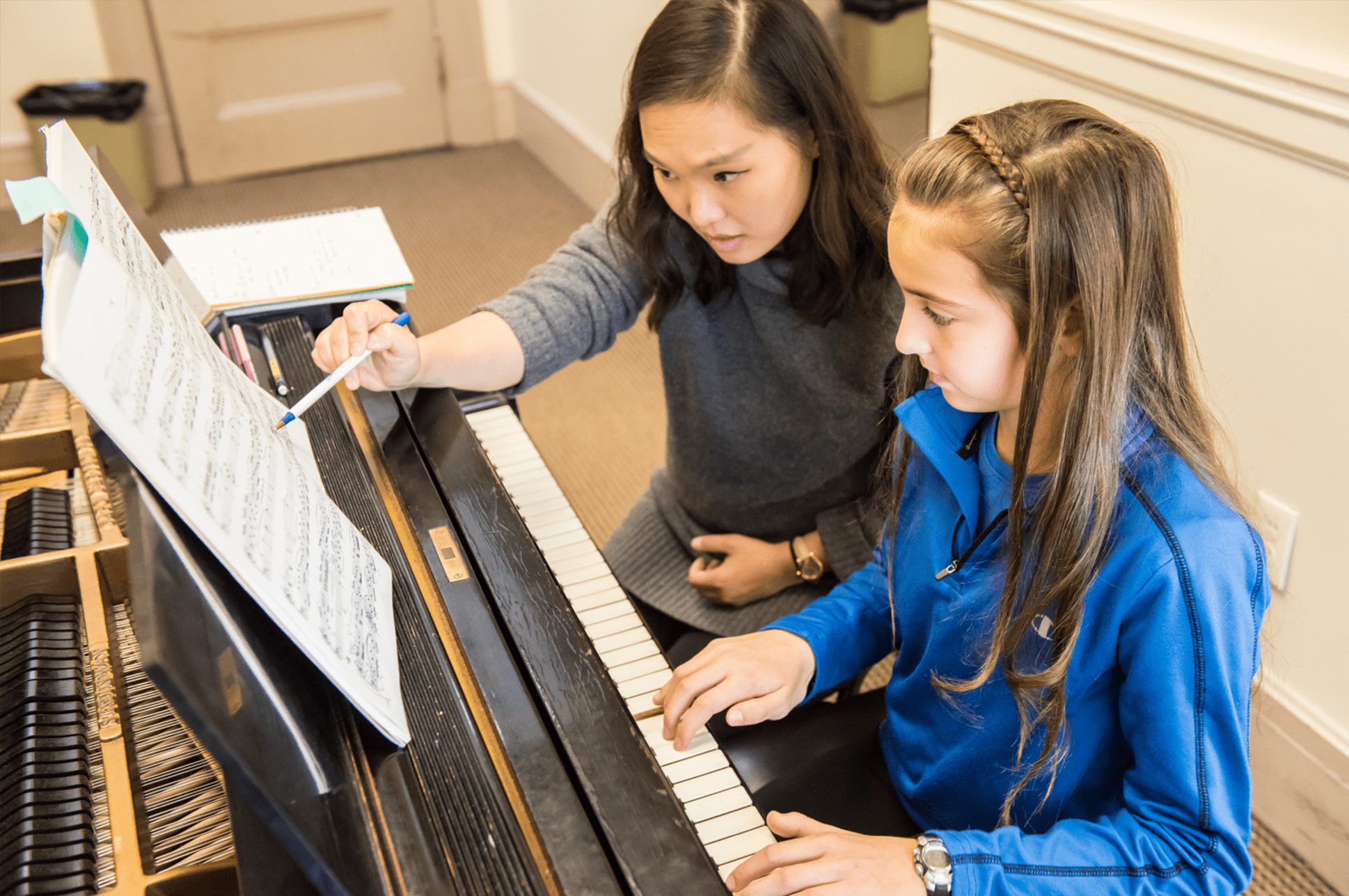 A piano teacher sitting at the piano with a student.