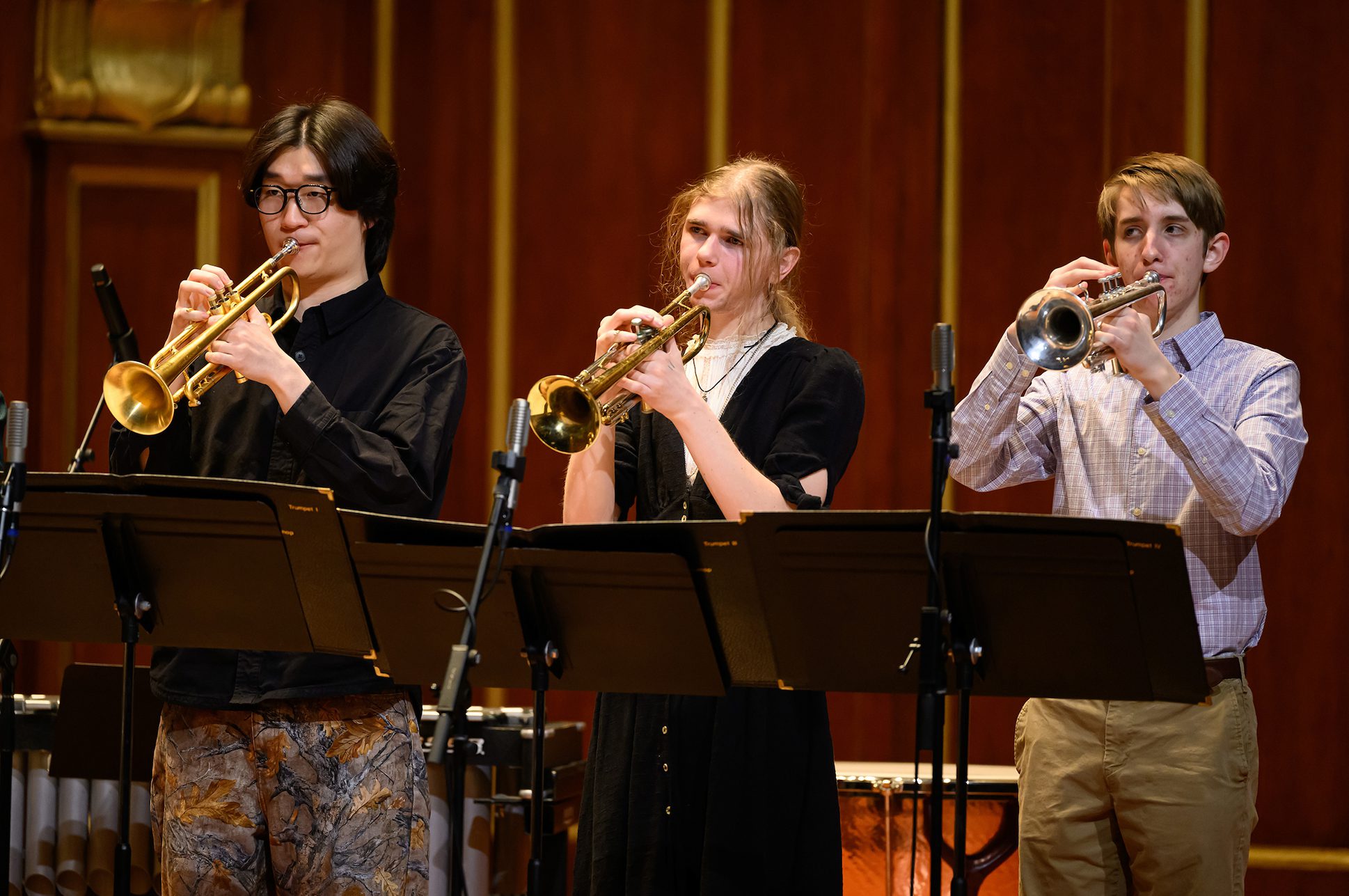 Three students playing the trumpet on the Jordan Hall stage.