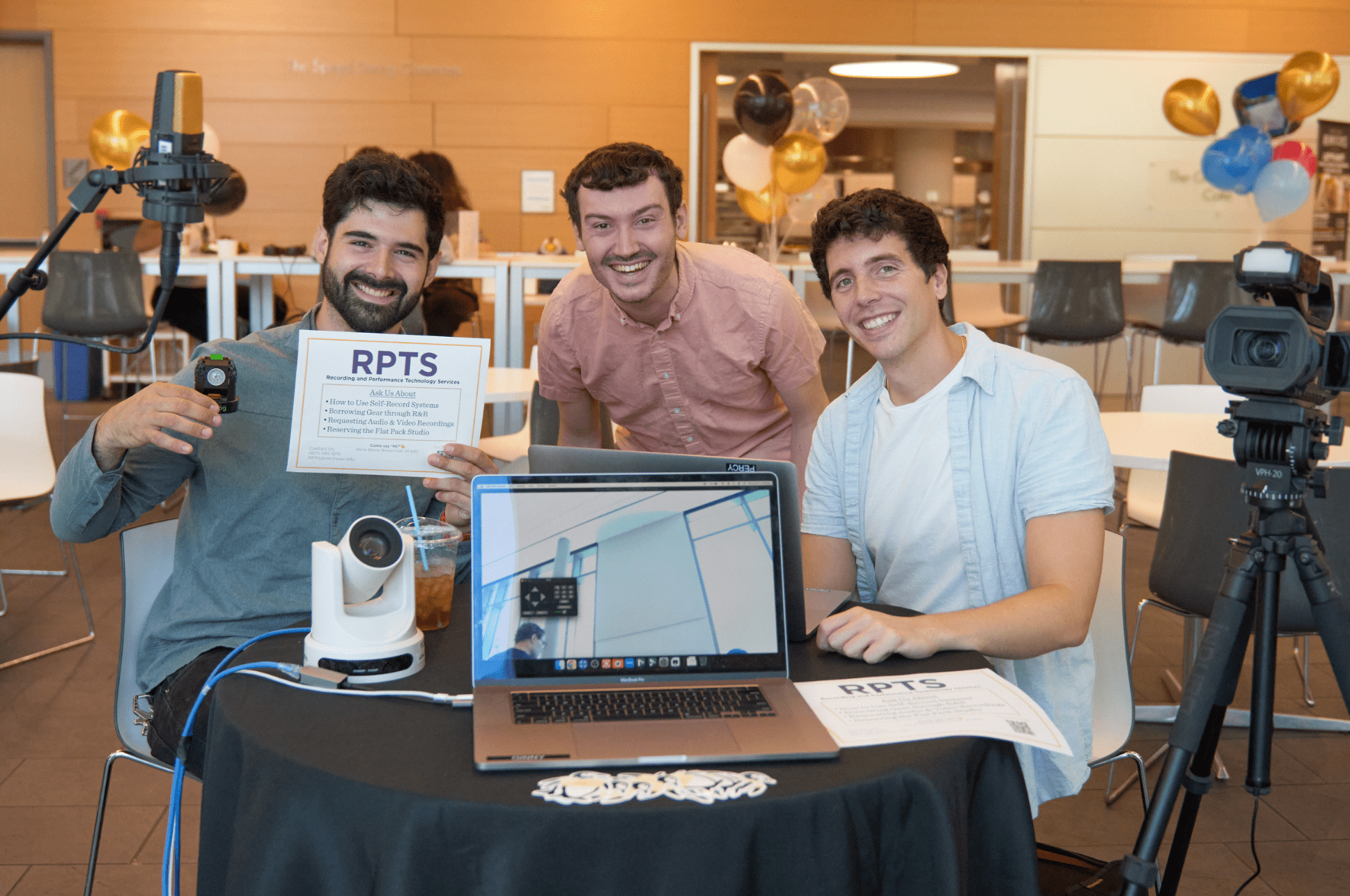 Three members of the NEC RPTS team sitting at a table with a laptop and audio/visual equipment.