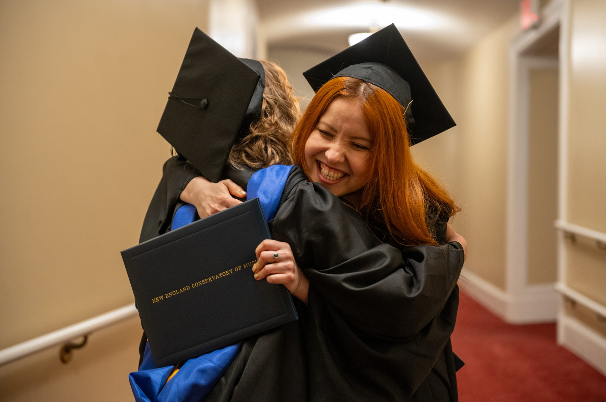 Two students in graduation regalia hugging.